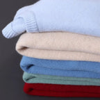 Pile de pulls en cachemire colorés, doux et élégants, comprenant des teintes bleu clair, beige, bleu, vert et rouge, sur fond gris.