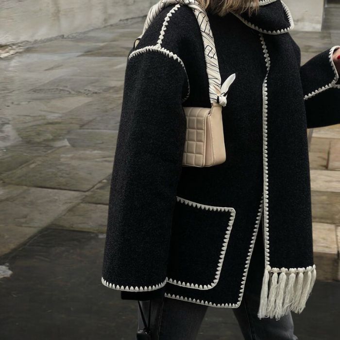 Manteau noir élégant avec bordures blanches, sac à main beige texturé, mode automne-hiver, style urbain chic, tendance vestimentaire moderne.