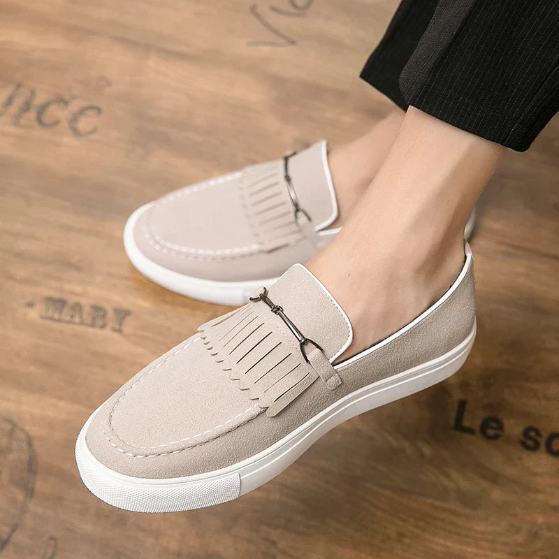 Chaussures mocassins beige pour homme sur sol en bois, design élégant avec franges, semelle blanche épaisse. Mode masculine, confort, style décontracté.