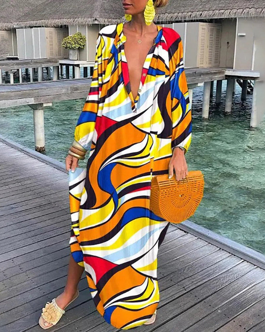 Robe longue colorée à motifs géométriques, femme tenant un sac en bambou, sandales beiges, fond de bungalows sur pilotis et mer turquoise.