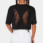 Femme portant un t-shirt noir avec motif ailes de papillon en dentelle au dos, coiffure tresses, pantalon blanc. Mode tendance, style unique.