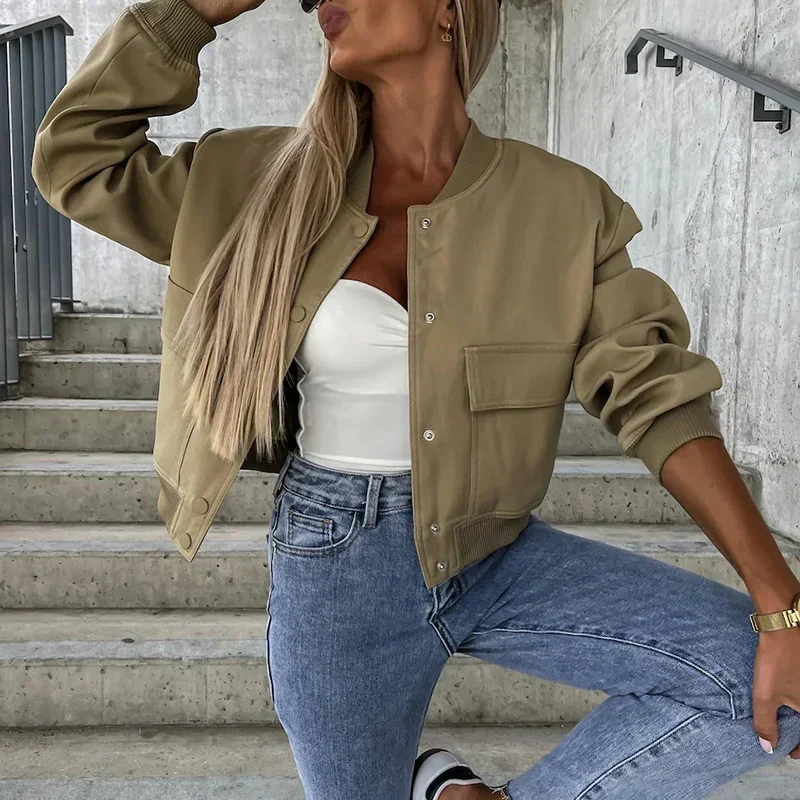 Femme en veste bomber beige, top blanc et jean bleu, posant sur des escaliers en béton. Mode décontractée, style urbain tendance.