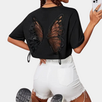 T-shirt noir avec motif ailes de papillon en dentelle, porté par une femme en short blanc. Mode tendance, style décontracté, été 2023.