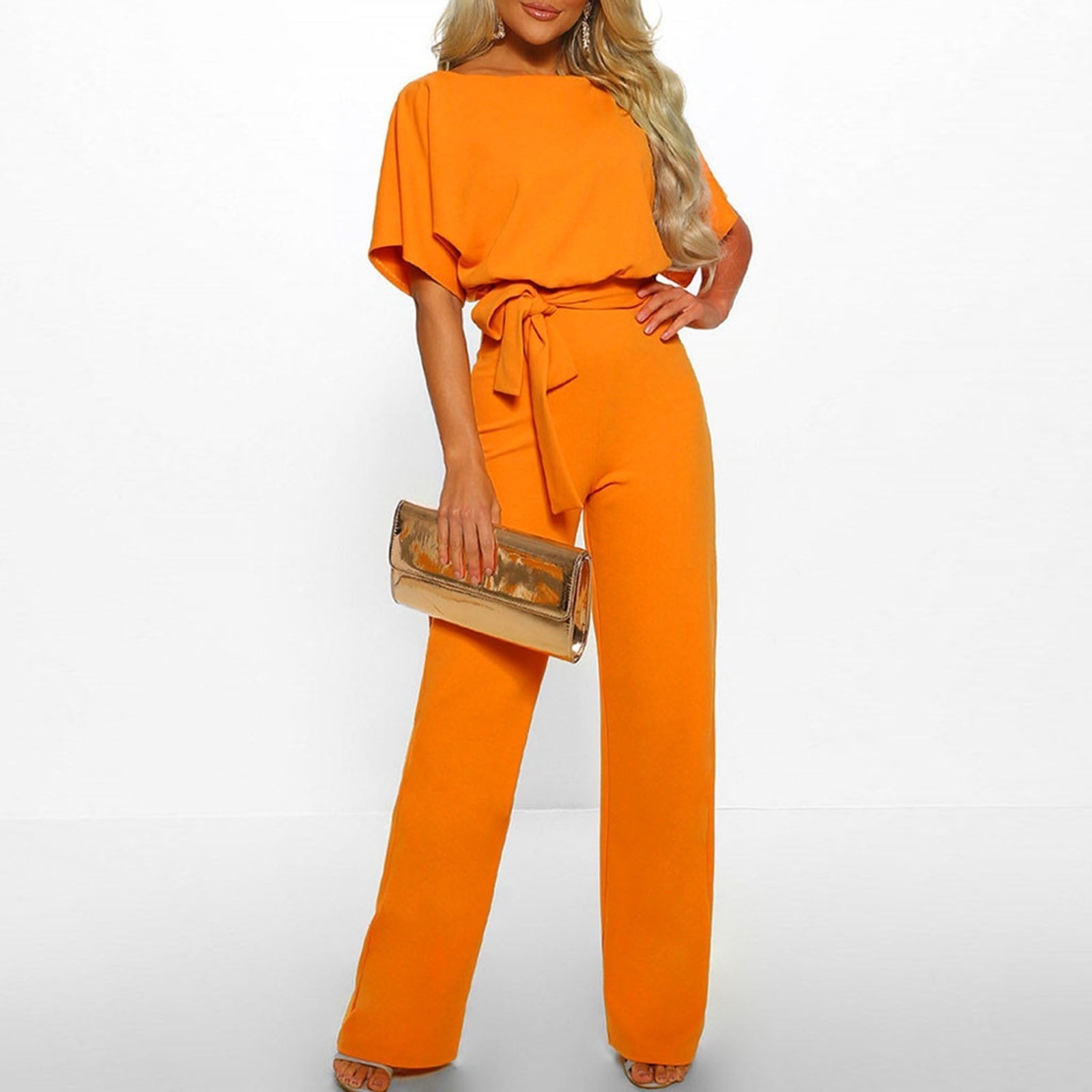 Femme en combinaison orange élégante avec ceinture, tenant une pochette dorée. Mode féminine chic, tenue de soirée tendance.