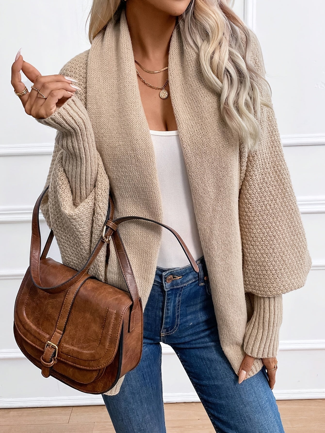 Femme portant un cardigan beige en maille, un débardeur blanc, un jean bleu et un sac à main en cuir marron. Mode automne chic et décontractée.
