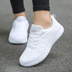 Chaussures de sport blanches pour femme sur trottoir, design léger et respirant, idéales pour la course et le fitness.