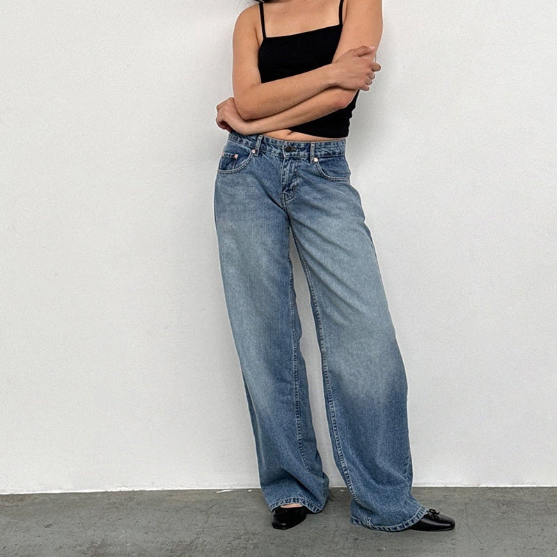 Femme en débardeur noir et jean large bleu, pose décontractée contre un mur blanc. Mode décontractée, tendance jeans larges, style minimaliste.