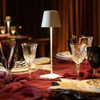 Table élégante avec lampe moderne, verres en cristal, nappes bordeaux, ambiance chaleureuse. Décoration de table raffinée pour dîner chic.