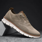 Chaussure de sport beige en maille respirante, semelle blanche antidérapante, posée sur un bloc gris. Idéale pour le confort et le style urbain.