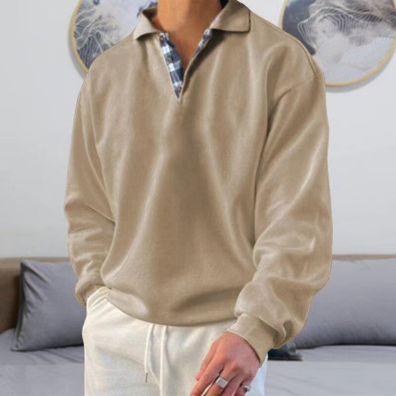 Homme portant un pull beige à col en V avec chemise à carreaux, pantalon blanc. Mode décontractée, style élégant, intérieur moderne.