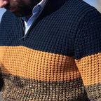 Homme portant un pull tricoté à rayures bleu marine, orange et marron, en extérieur. Mode hiver, style décontracté, vêtements chauds.