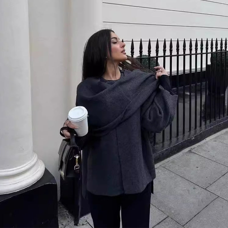 Femme élégante tenant un gobelet de café, portant un manteau gris, posant devant une clôture en fer forgé. Mode urbaine, style automnal.