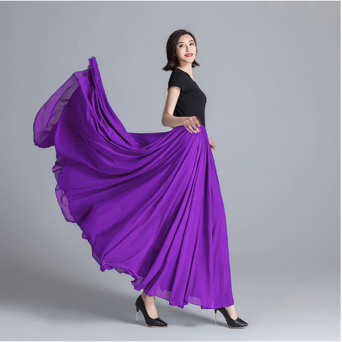 Femme en robe longue violette fluide, posant élégamment sur fond gris. Mode féminine, élégance, style chic, robe de soirée tendance.