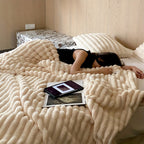 Femme dormant sur un lit avec couverture en fausse fourrure beige, tablettes posées à côté, chambre moderne. Confort, détente, literie luxueuse.