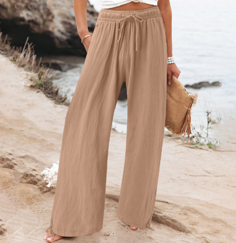 Pantalon large beige femme, style décontracté, bord de mer, accessoire sac paille, mode estivale, tenue plage élégante et confortable.
