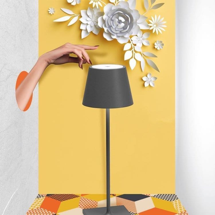 Lampe moderne grise sur fond jaune avec fleurs en papier blanc, main féminine ajustant l'abat-jour, design intérieur élégant et créatif.