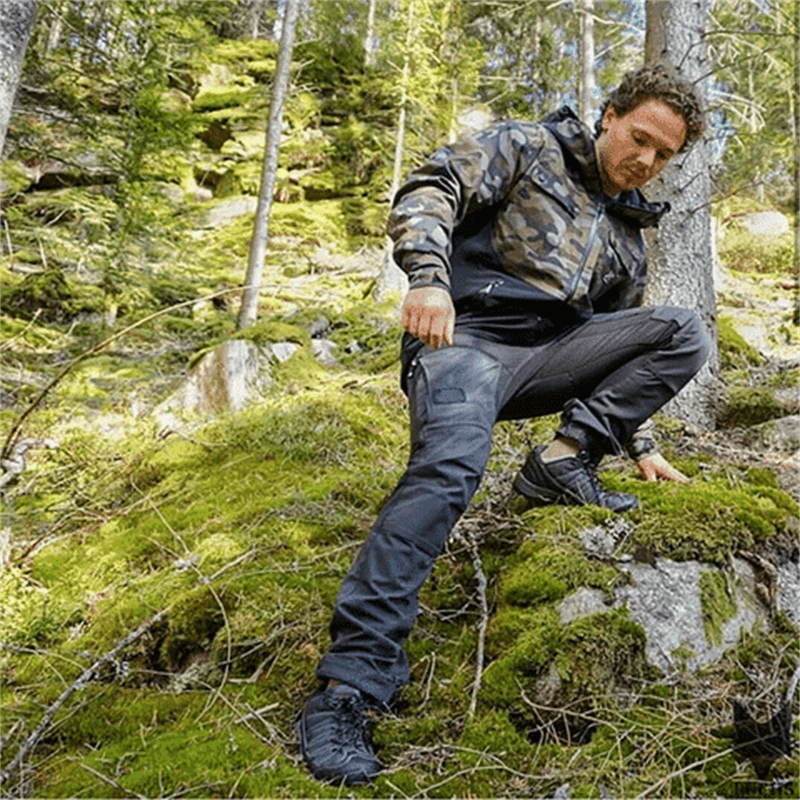 Homme en tenue camouflage randonnée dans forêt verdoyante, portant veste imperméable et pantalon résistant, explorant nature sauvage.
