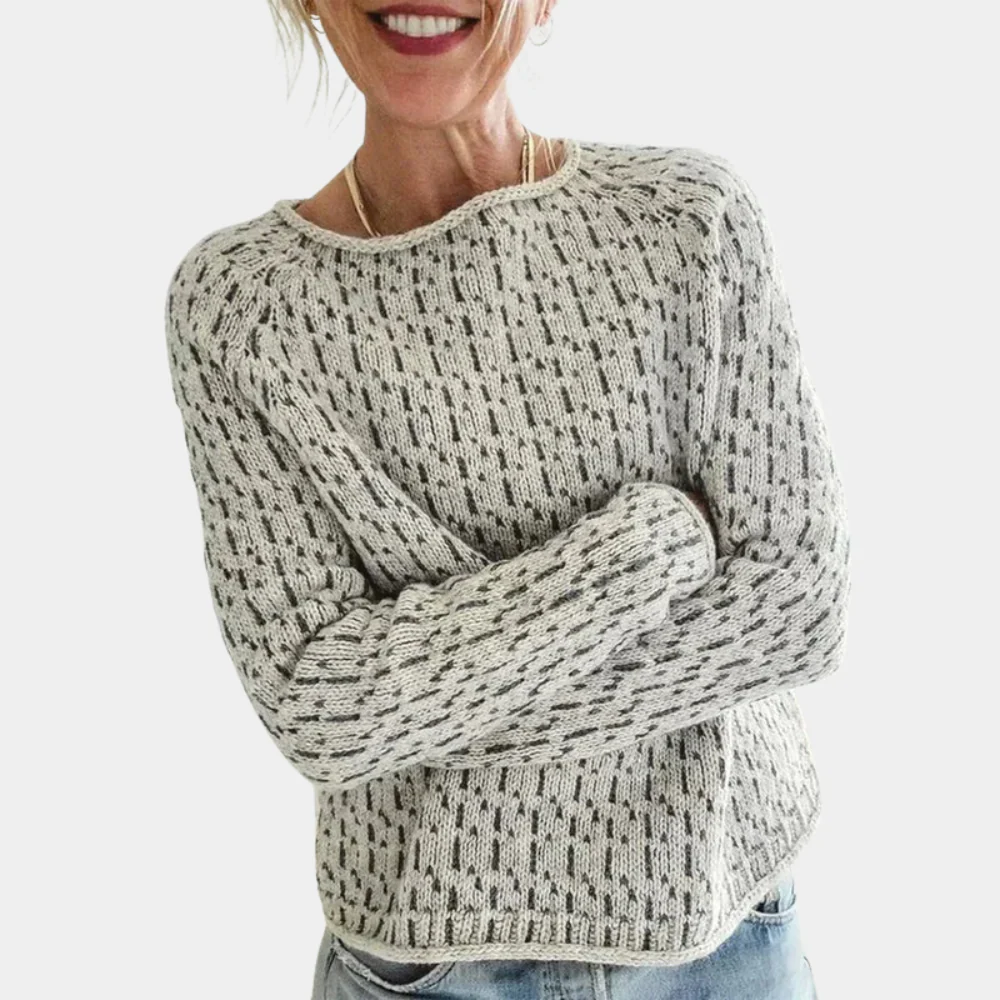 Femme souriante portant un pull en laine gris à motifs, manches longues, col rond, style décontracté, avec un jean bleu clair.