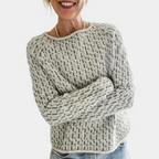Femme souriante portant un pull en laine gris à motifs, manches longues, col rond, style décontracté, avec un jean bleu clair.