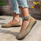 Chaussures plates beiges en maille sur pieds féminins, portées avec un jean déchiré et bracelets de cheville turquoise, posées sur un sol en bois.