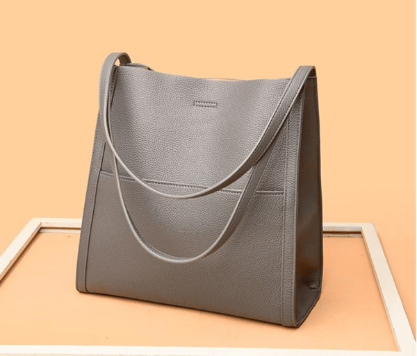 Sac à main en cuir gris élégant sur fond orange, design minimaliste, idéal pour la mode féminine, accessoire tendance et pratique.