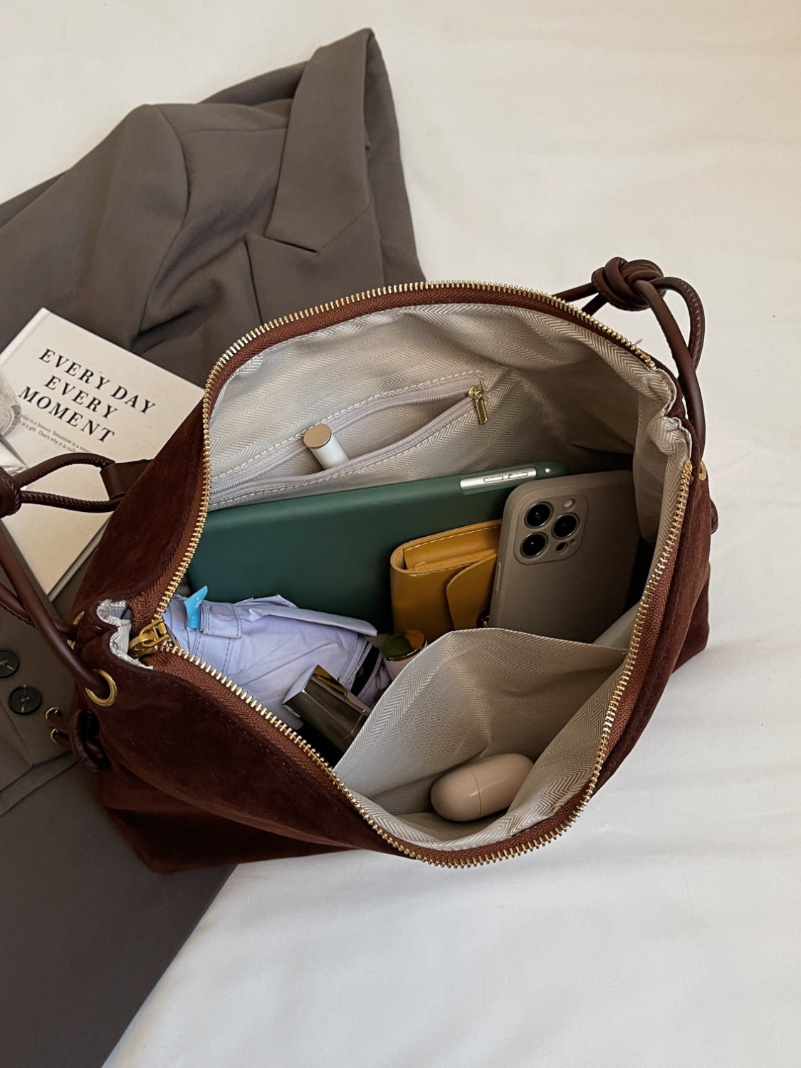 Sac à main en cuir marron ouvert, contenant un smartphone, portefeuille jaune, livre, et divers accessoires. Mode, accessoires femme, organisation.