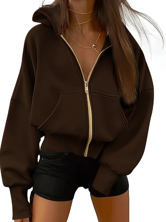 Femme portant un sweat à capuche marron foncé avec fermeture éclair dorée, collier doré, et short noir. Mode automne, style décontracté.