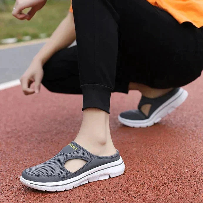 Personne portant des chaussures de sport grises sur une piste rouge. Chaussures légères, confortables, idéales pour la marche et le jogging.