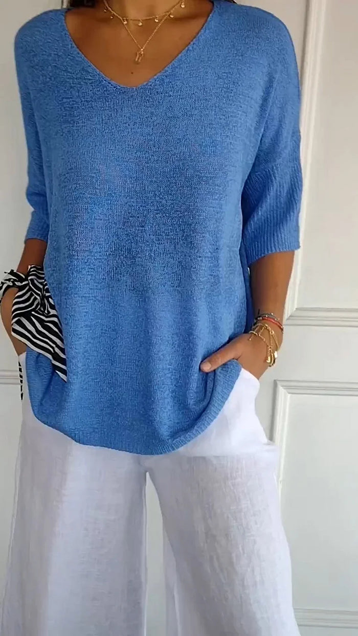 Femme portant un pull bleu ample avec un pantalon blanc, accessoirisé d'un foulard rayé noir et blanc. Mode décontractée élégante.