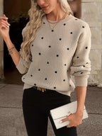 Femme portant un pull beige à pois noirs, tenant une pochette blanche. Mode automne, style décontracté chic, tendance féminine élégante.