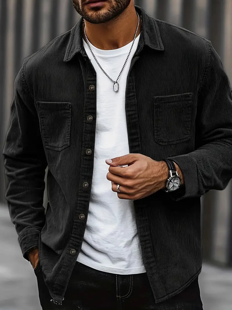 Homme portant une chemise noire en velours côtelé, t-shirt blanc, montre élégante et collier argenté. Mode masculine décontractée et tendance.