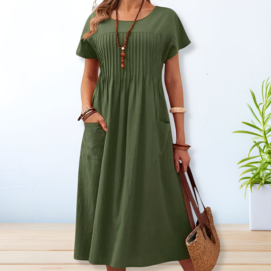 Robe verte longue en lin avec manches courtes, poches avant, et col rond. Accessoires: collier, bracelets, sac en osier. Style décontracté et estival.