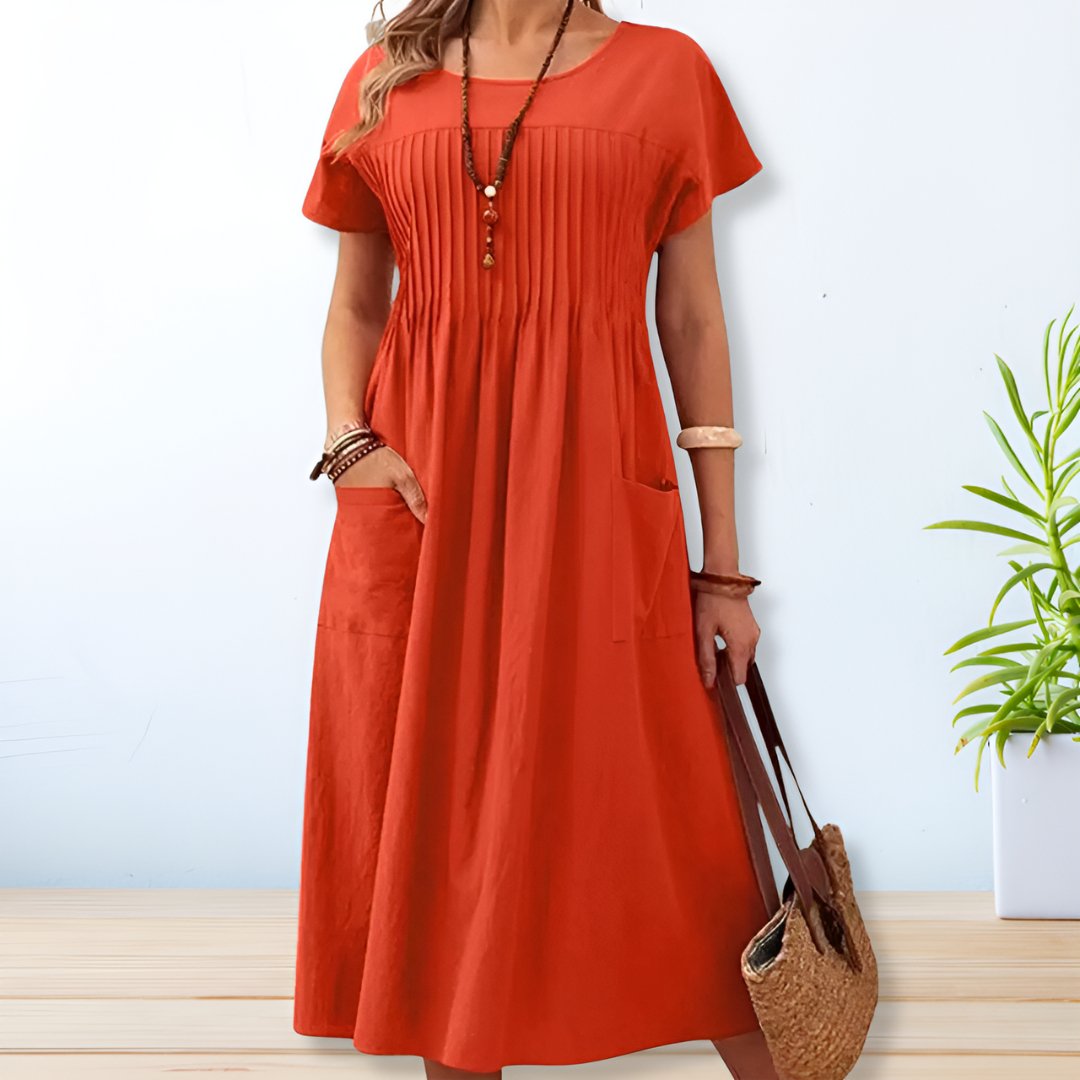 Robe longue orange à manches courtes avec poches, portée par une femme tenant un sac en osier. Style décontracté, idéal pour l'été.