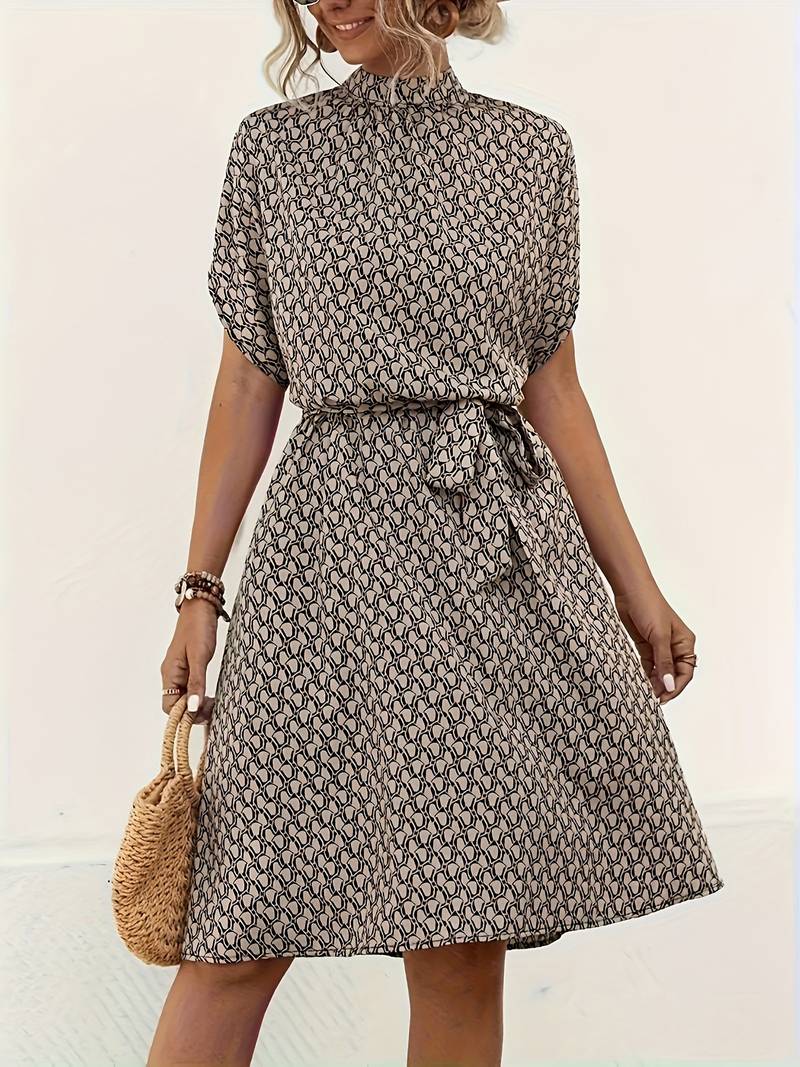 Robe d'été imprimée à motifs géométriques, manches courtes, ceinture nouée, femme tenant un sac en osier. Mode féminine élégante et décontractée.