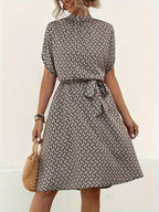 Robe d'été imprimée à motifs géométriques, manches courtes, ceinture nouée, femme tenant un sac en osier. Mode féminine élégante et décontractée.