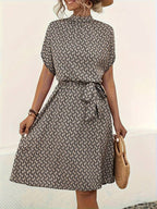 Robe d'été imprimée à motifs géométriques, ceinturée à la taille, portée par une femme avec un chapeau et un sac en osier. Mode féminine élégante.