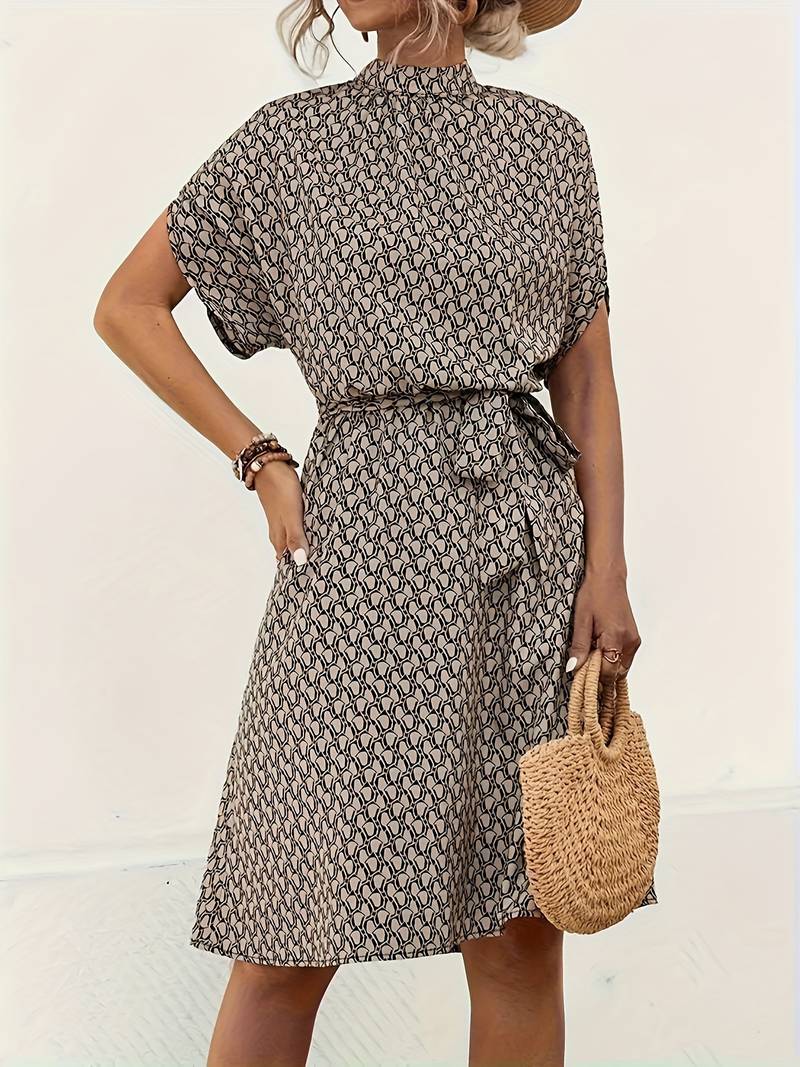 Robe d'été à motifs géométriques, manches courtes, ceinture nouée, portée par une femme avec un sac en osier. Mode féminine élégante et tendance.