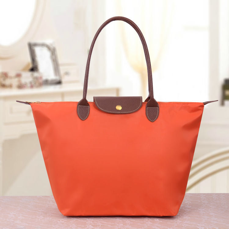 Sac à main orange vif avec poignées marron, posé sur une table. Design élégant et moderne, idéal pour la mode féminine et les accessoires tendance.