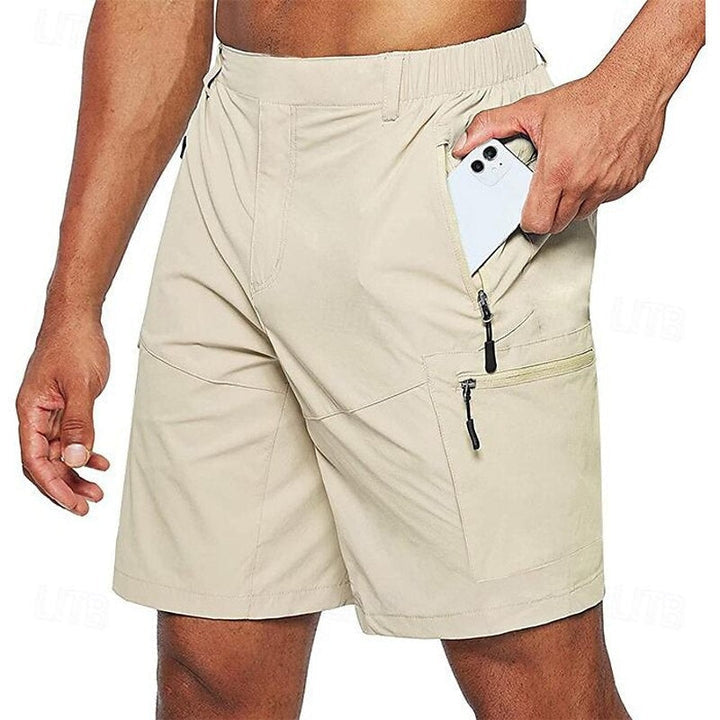 Homme portant un short beige avec poches zippées, tenant un smartphone. Mode masculine, short d'été, vêtement pratique.