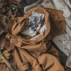 Veste en toile marron avec capuche, doublure imprimée, posée sur des vêtements de travail. Style vintage, mode utilitaire, vêtements durables.