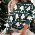 Femme portant un pull de Noël vert avec motifs sapins blancs, assise près d'un sapin décoré. Mode hiver, tendance festive, vêtements chauds.
