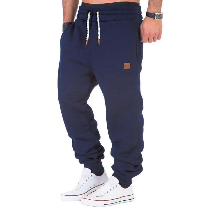 Pantalon de jogging bleu marine pour homme, avec cordons blancs et poches, porté avec des baskets blanches. Mode décontractée et confortable.