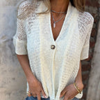 Femme portant un cardigan en maille crème avec un bouton, collier en chaîne argentée et bracelets dorés, mode décontractée élégante.