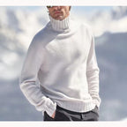 Homme portant un pull blanc à col roulé en laine, debout dans un paysage enneigé. Mode hiver, vêtements chauds, style élégant.