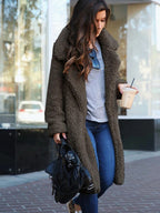 Femme portant un manteau en fausse fourrure marron, jeans bleu, tenant un café glacé et un sac noir, marchant en ville. Mode automne-hiver tendance.