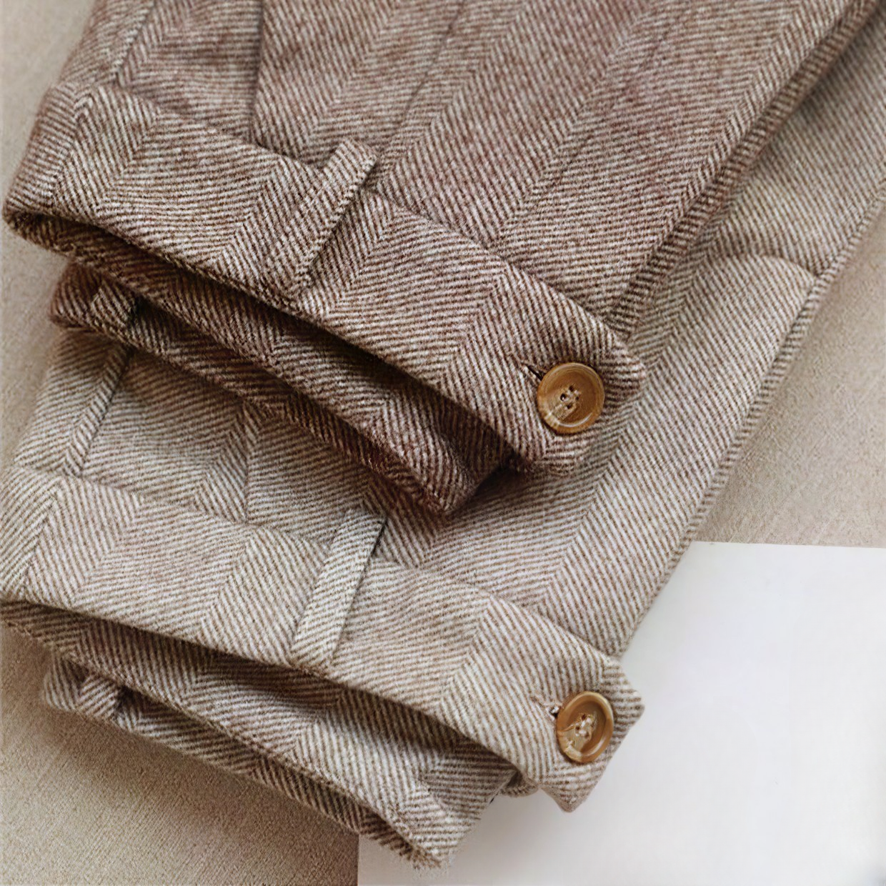 Pantalons en tweed marron clair pliés, boutons en bois, motif chevrons, tissu élégant et texturé, mode automne-hiver, style classique et intemporel.