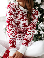 Femme portant un pull de Noël rouge et blanc avec motifs de rennes et flocons, assise devant un sapin décoré. Mode festive hiver.