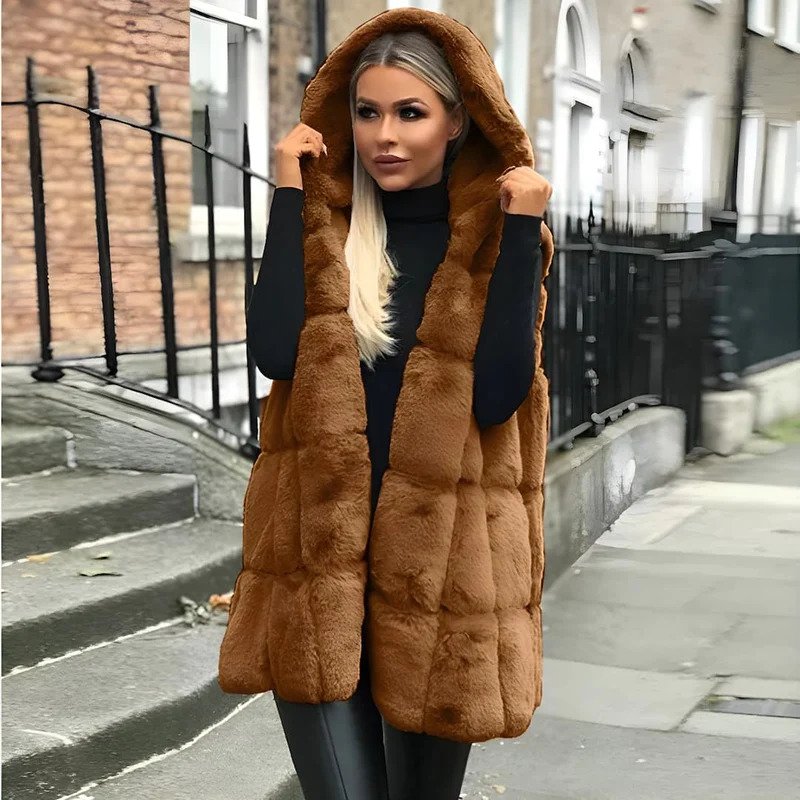 Femme portant un gilet en fausse fourrure marron avec capuche, tenue élégante d'hiver, rue pavée en arrière-plan. Mode automne-hiver tendance.