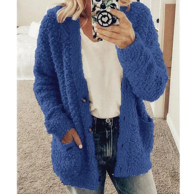 Femme portant un cardigan bleu en tricot texturé, t-shirt blanc et jean, tenant un smartphone. Mode automne-hiver, tenue décontractée tendance.