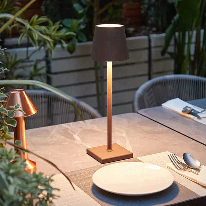Lampe de table moderne en métal sur une terrasse élégante, entourée de plantes vertes. Décoration extérieure chic, ambiance chaleureuse et conviviale.
